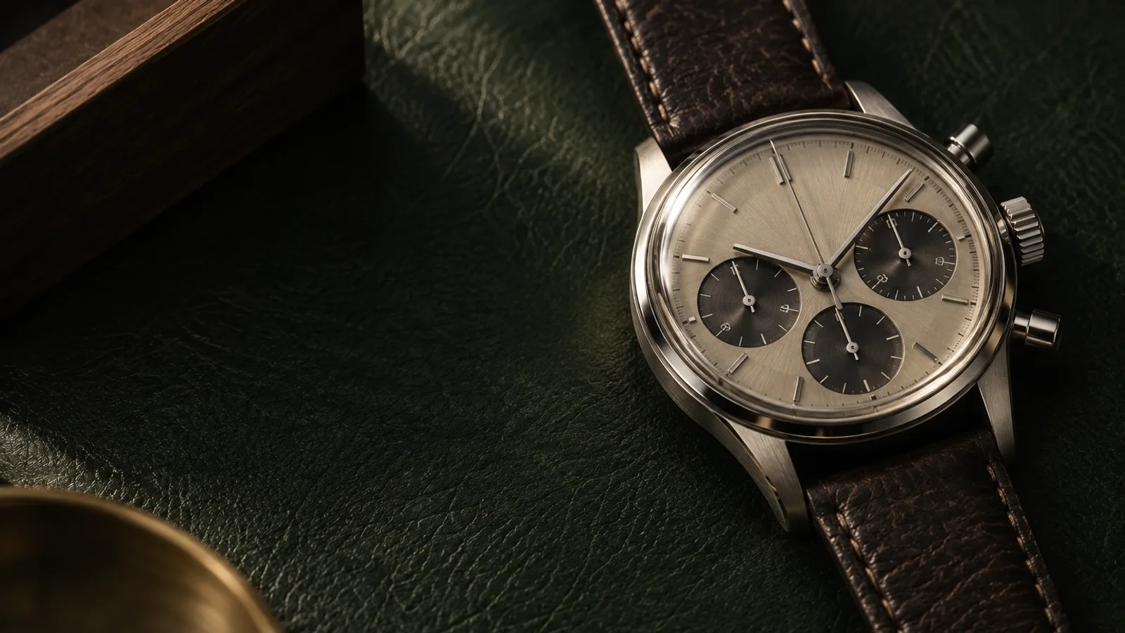 Nahaufnahme eines mechanischen Chronographen auf dunkelgrünem Leder, beleuchtet von warmem Licht.